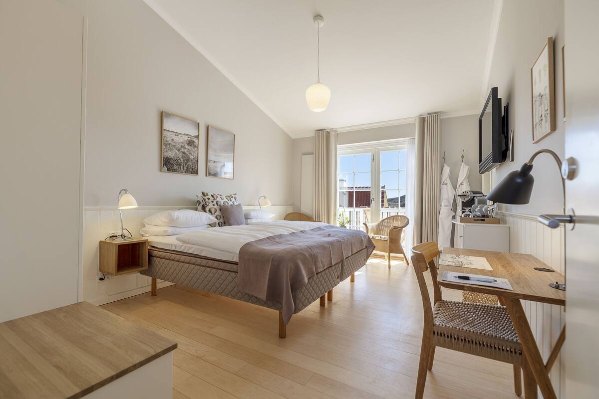 A modern bedroom with a bed, bedside table, lamp, chair, and a desk with a chair.