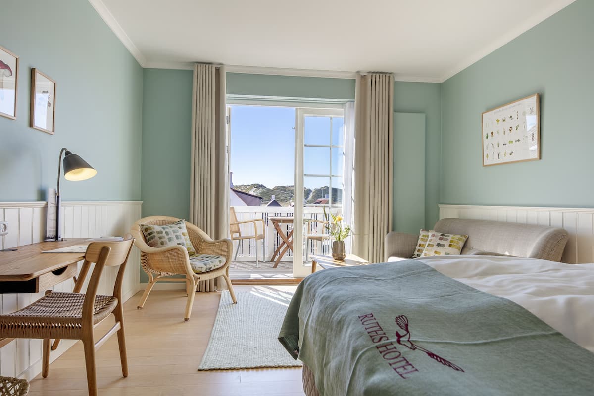A hotel room with a bed, a desk, a chair, and a balcony with a view.