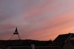 A sunset over a town with a prominent tower structure and traditional buildings with red-tiled roofs.