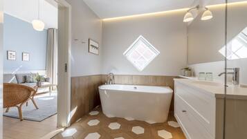 Un baño moderno con una bañera independiente, un espejo grande y una ventana sobre el lavabo.
