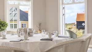 A dining area with a table set for four, white chairs, and a view of the outside. - Ruths Hotel (Skagen)