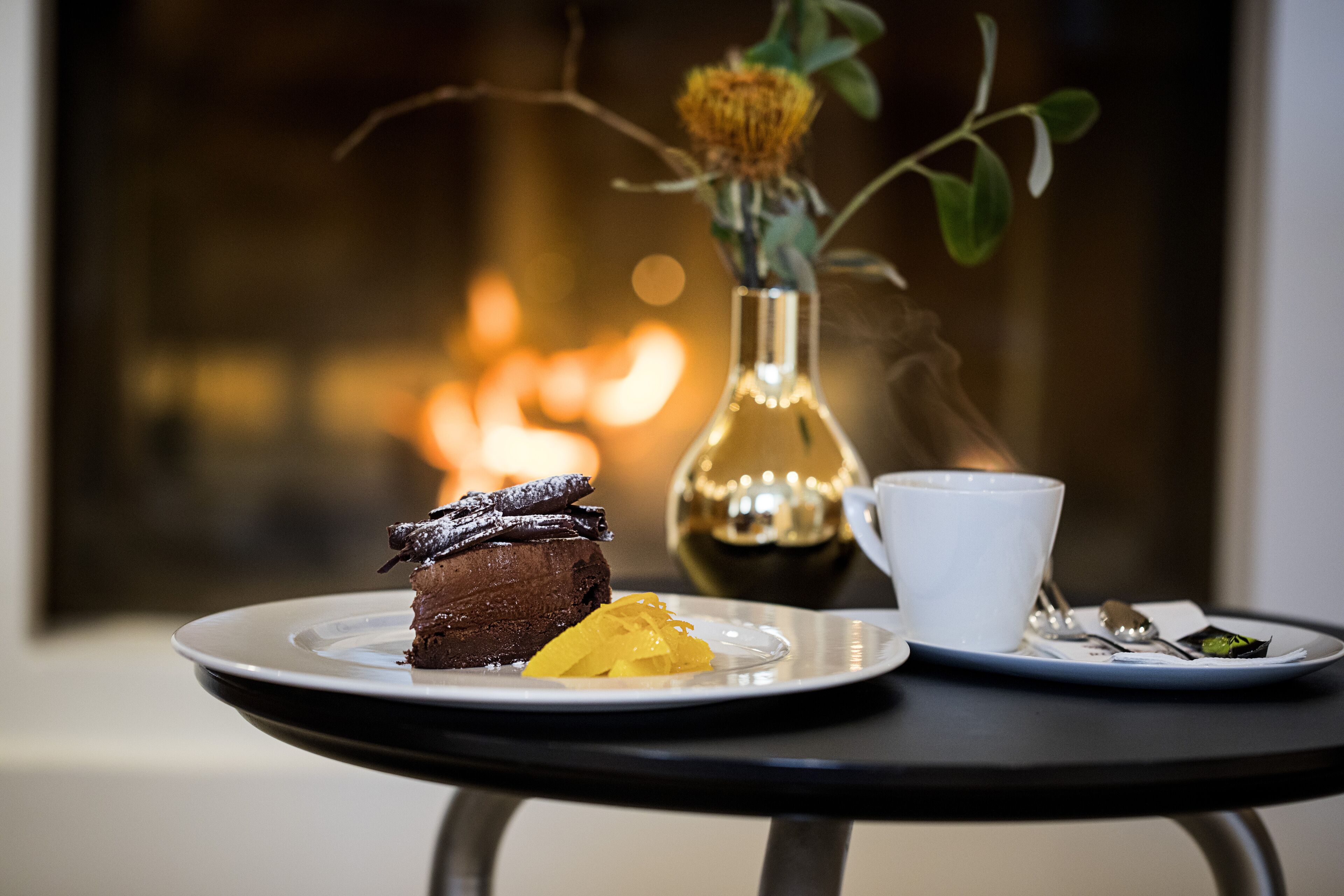 Um prato de sobremesa com bolo de chocolate e uma fruta amarela sobre uma mesa com uma xícara branca e uma colher.
