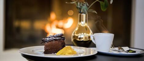 A dessert plate with a chocolate cake and a yellow fruit on a table with a white cup and a spoon.