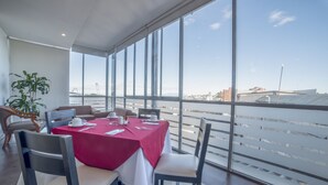 Un comedor moderno con mantel rojo, sillas blancas y vistas a un puente y al paisaje urbano a través de amplios ventanales.