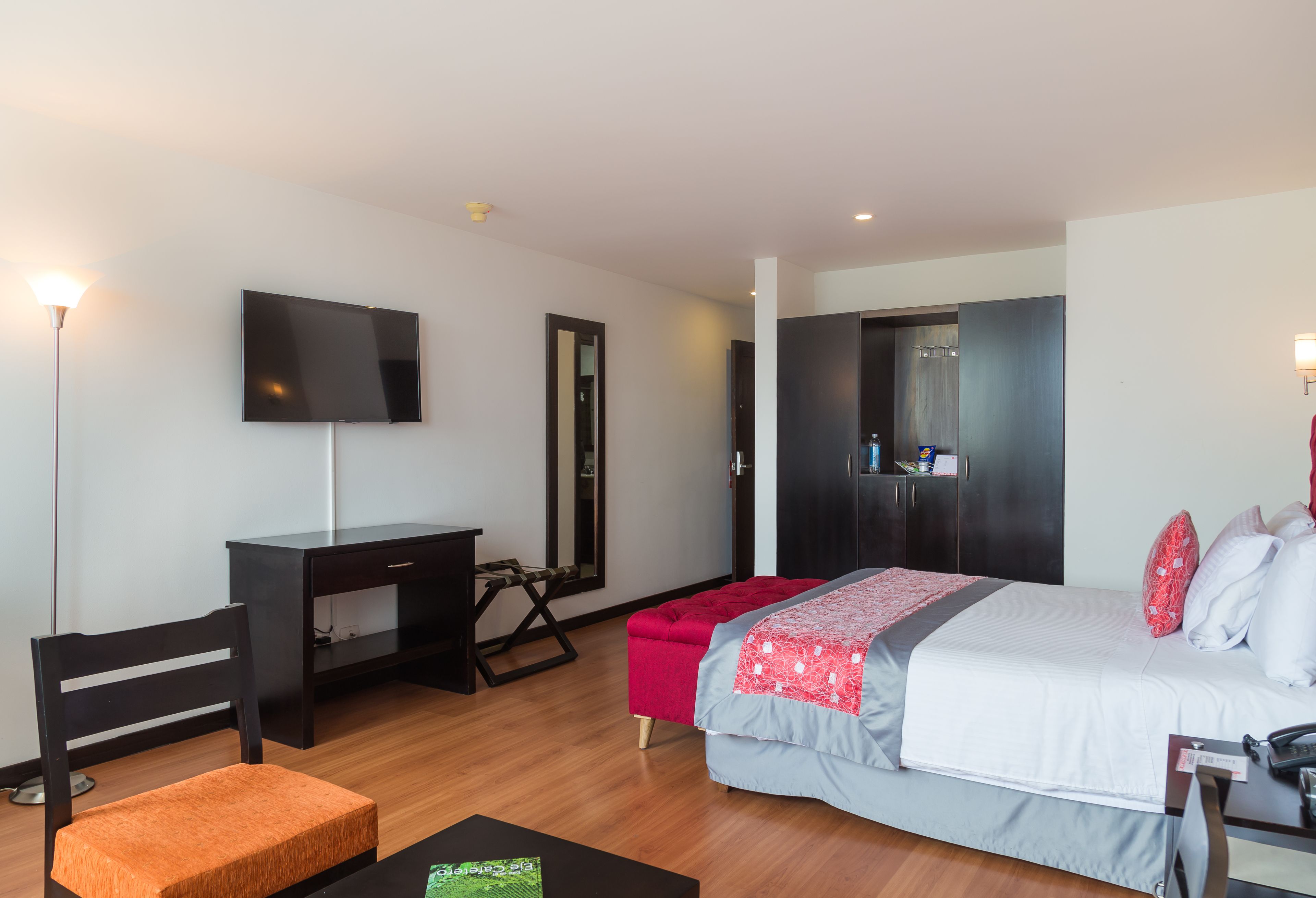 Quarto de hotel moderno com cama, escrivaninha, cadeira e televisão.