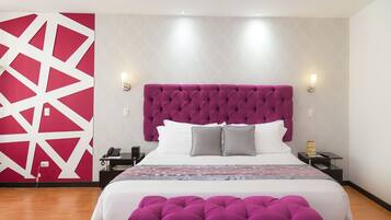 A modern hotel room with a large bed, a tufted headboard, two bedside lamps, a nightstand, and a decorative wall panel.