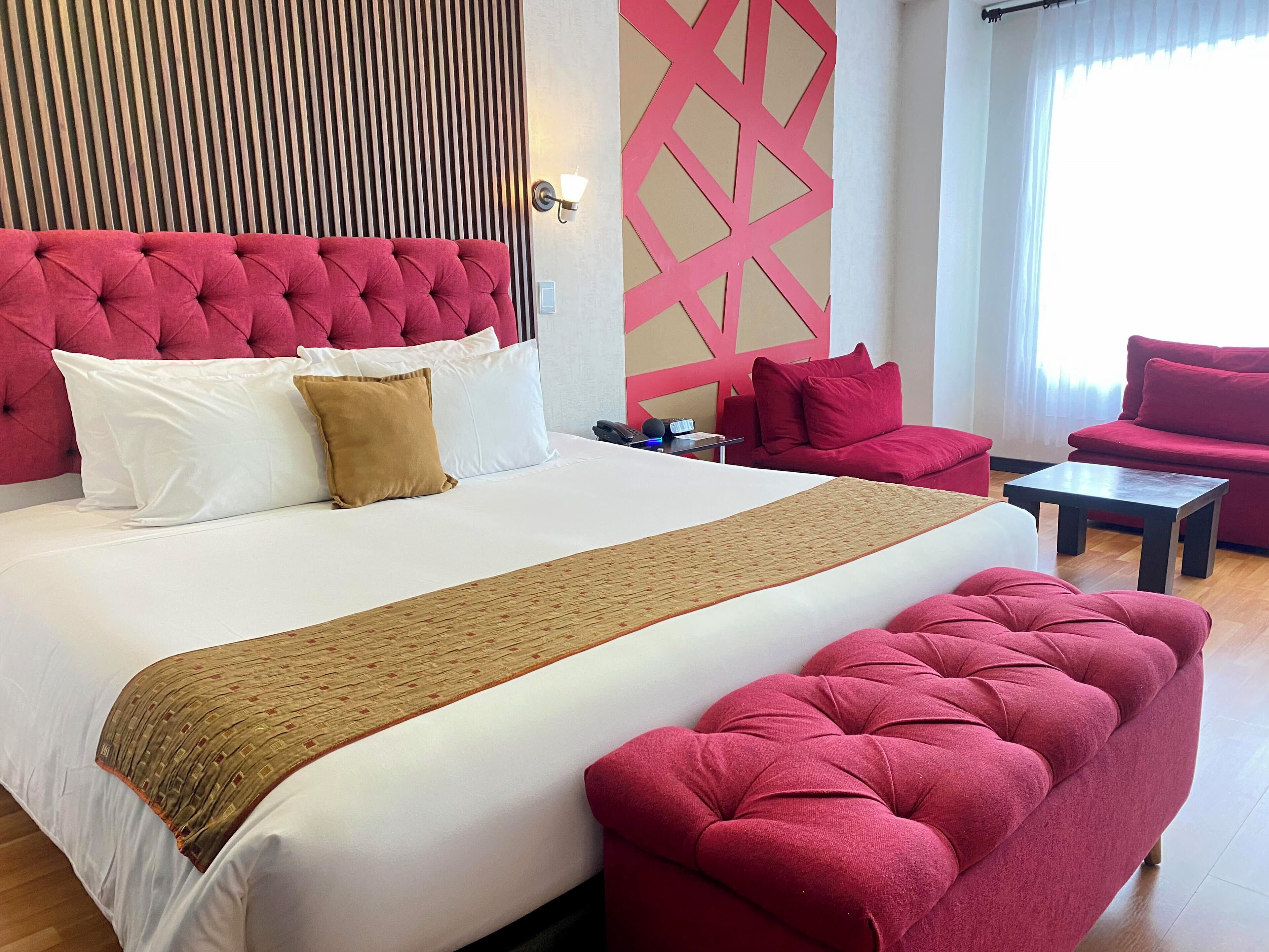Hotellihuone, jossa on suuri sänky, punaisella kankaalla verhoiltu pääty ja samanväriset punaiset huonekalut.