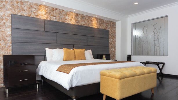 Un dormitorio moderno con una cama grande, una mesita de noche, un banco y un adorno en la pared.