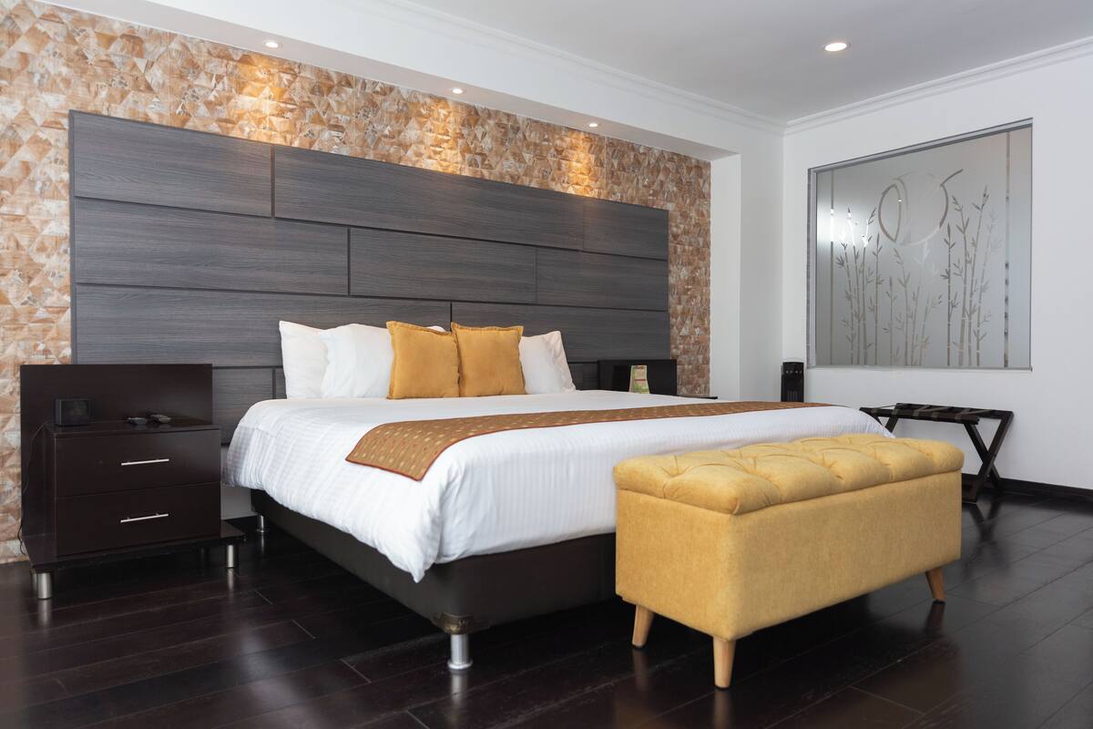 A modern bedroom with a large bed, a nightstand, a bench, and a decorative wall.