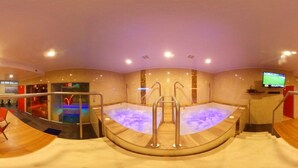Un área de spa con una bañera de hidromasaje, un televisor y una zona de estar con sillones rojos.
