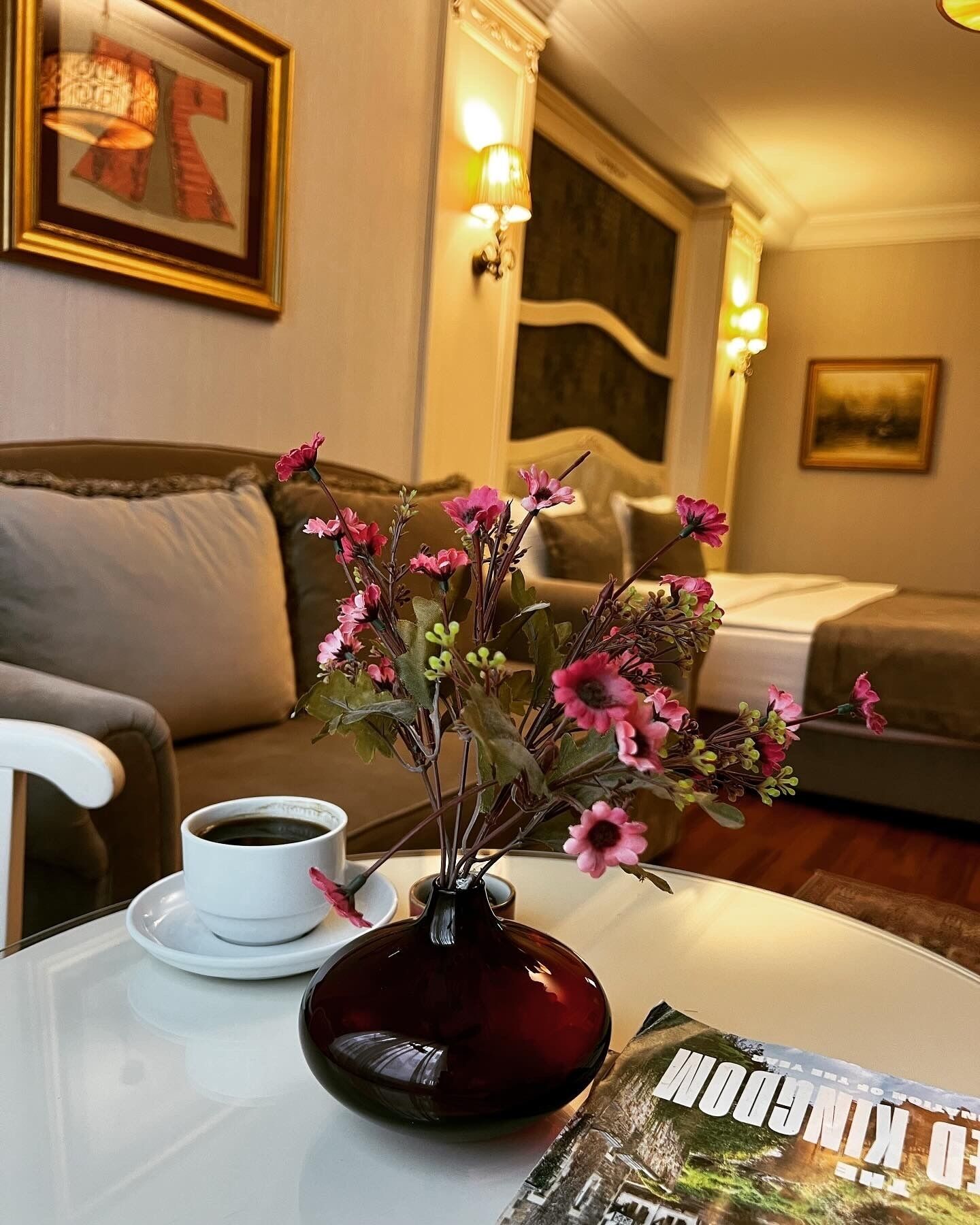 A room with a sofa, a coffee cup on a table, a vase with flowers, and a framed picture on the wall.