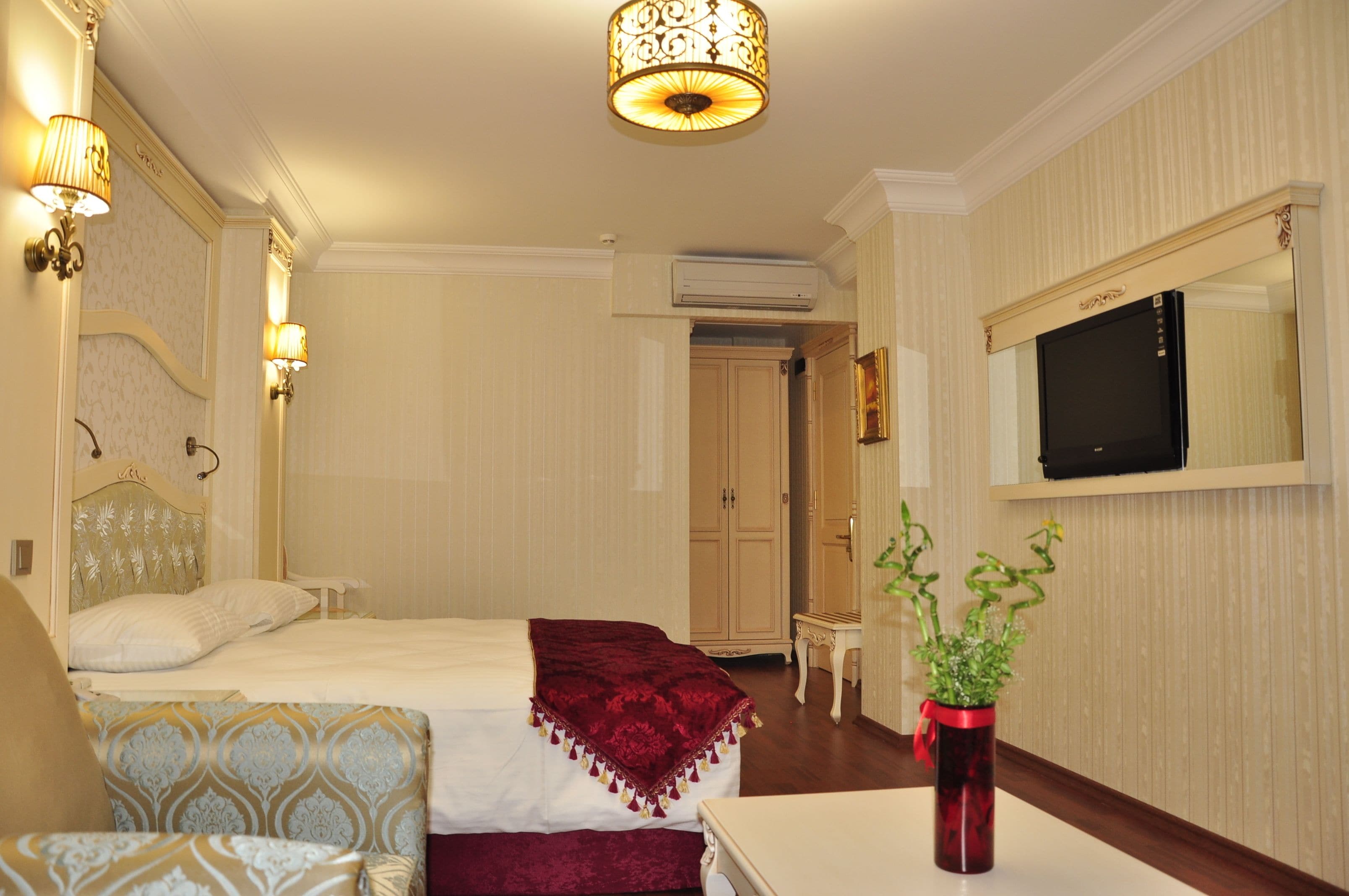 Une chambre d’hôtel avec un lit, des lampes de chevet, une télévision, un miroir, une plante et une petite table.
