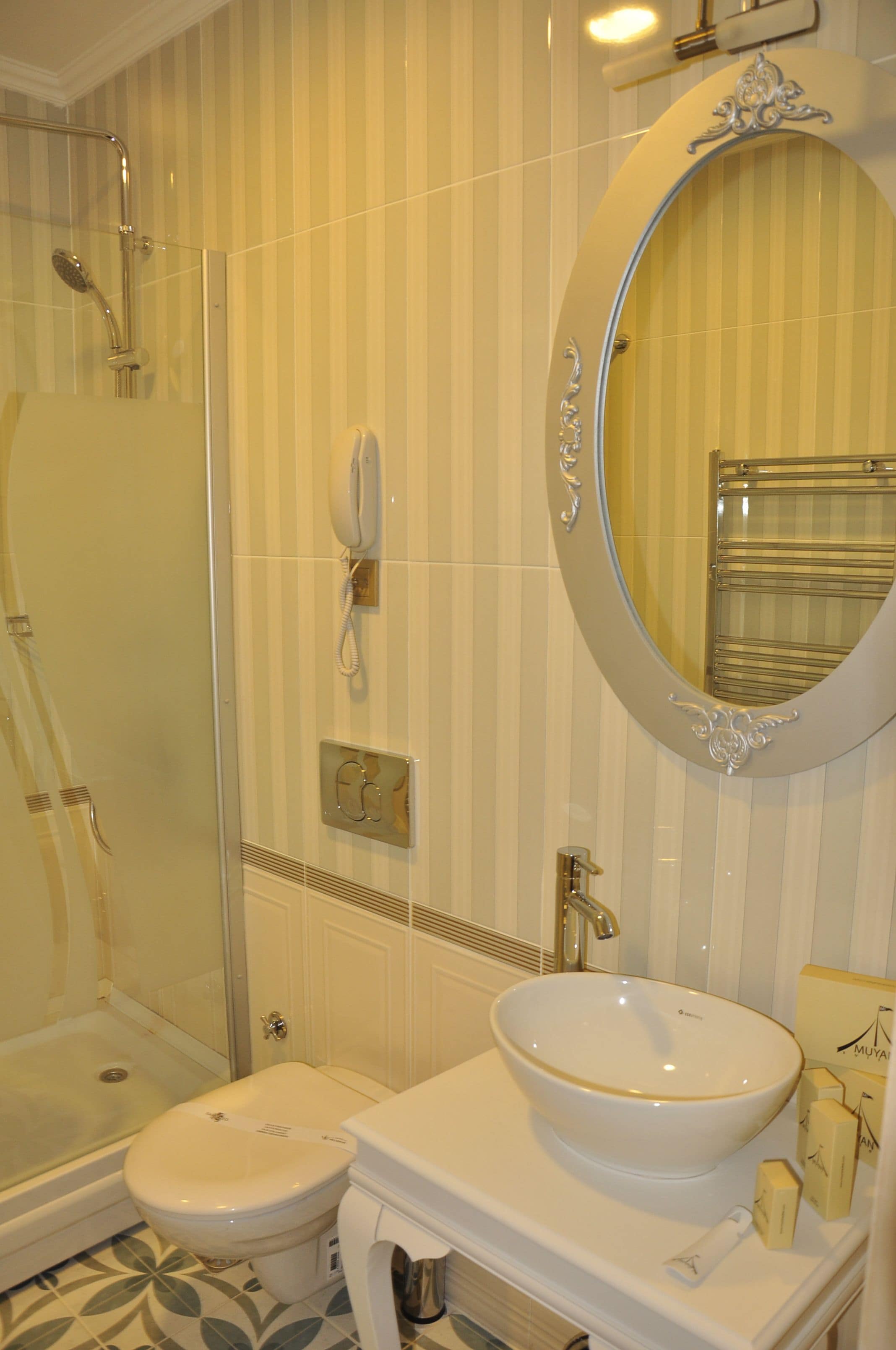 A bathroom with a glass-enclosed shower, a white toilet, and a large oval mirror above a white sink.