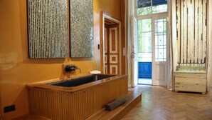 Una bañera de madera en una habitación con suelo de madera, una puerta y un ventanal con vistas.