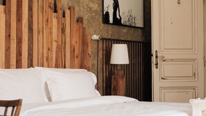 Un dormitorio con cabecera de madera, cama blanca, una mesa de madera y una puerta.