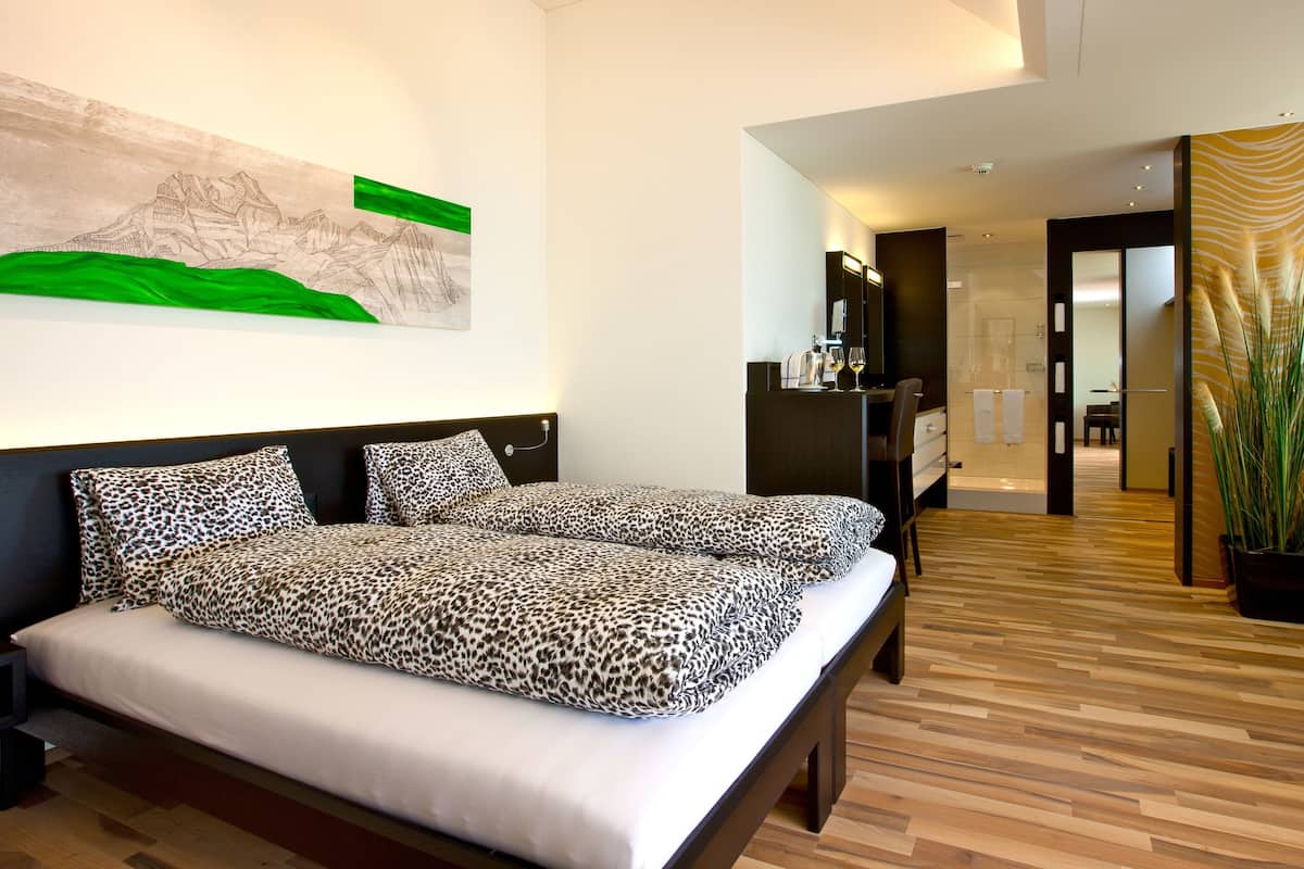 Un dormitorio moderno con cama, escritorio y baño visible a través de una puerta abierta.