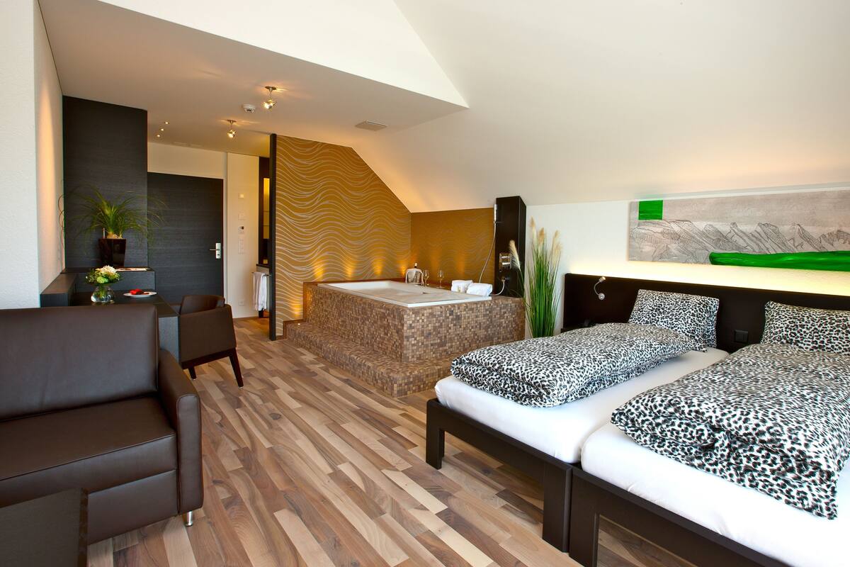 Una habitación de hotel moderna con una cama grande, un área de estar separada, una bañera y vistas a las montañas.