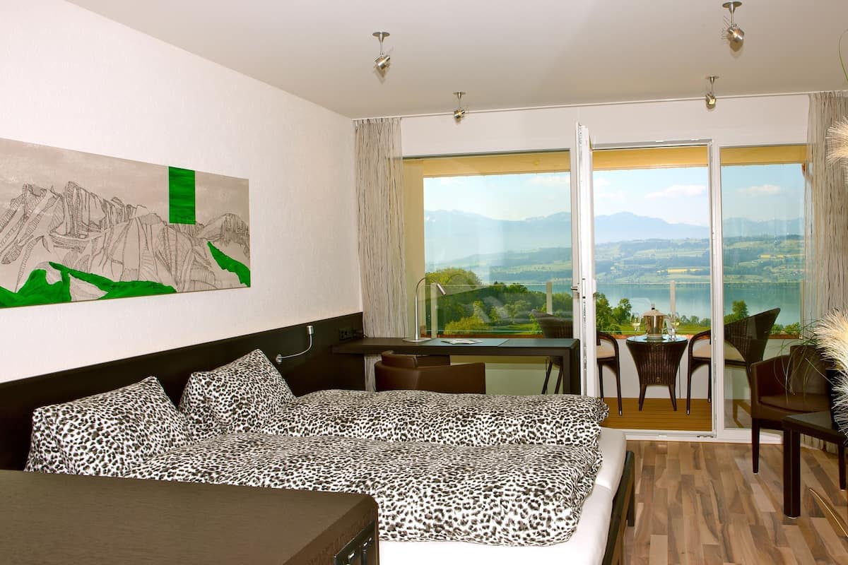 Un dormitorio con cama, escritorio y vistas a un lago y montañas.