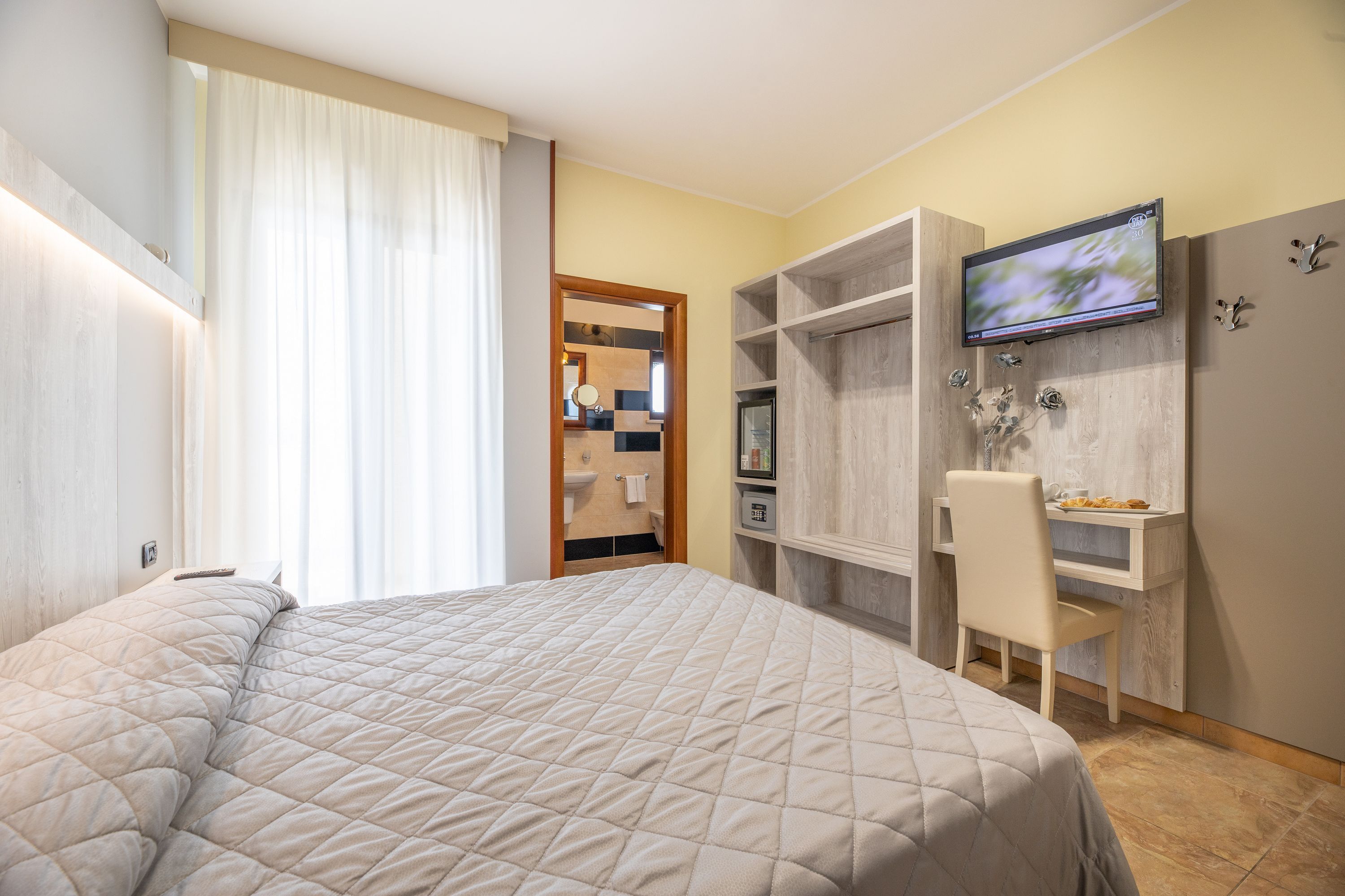 Quarto com cama, escrivaninha e televisão.