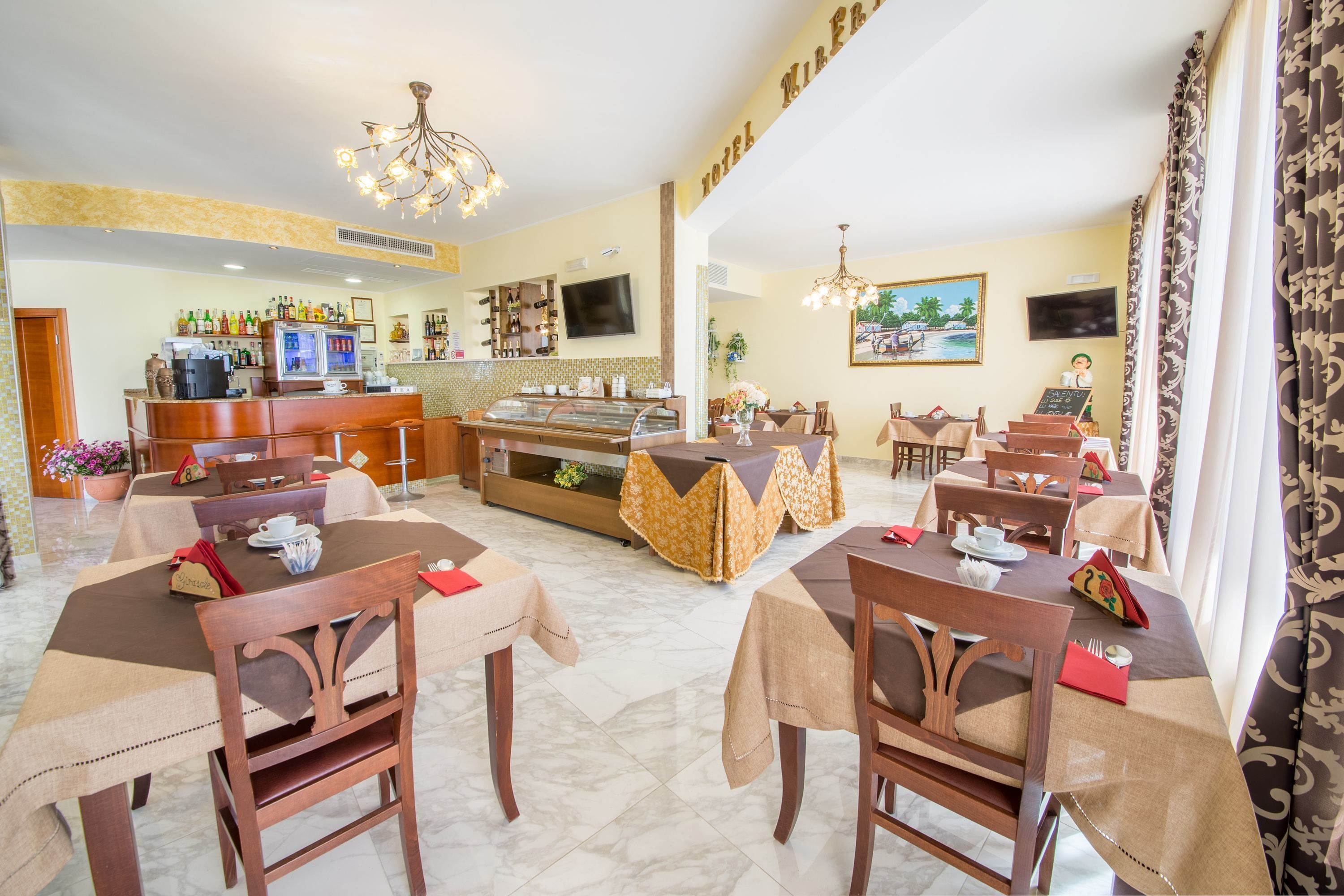 Un comedor de hotel con varias mesas, sillas, una barra y una pantalla de televisión.