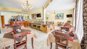 Un comedor de hotel con varias mesas, sillas, una barra y una pantalla de televisión.