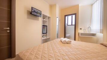 Una camera da letto con un letto, una televisione su uno scaffale, l'ingresso del bagno e una finestra con tende.