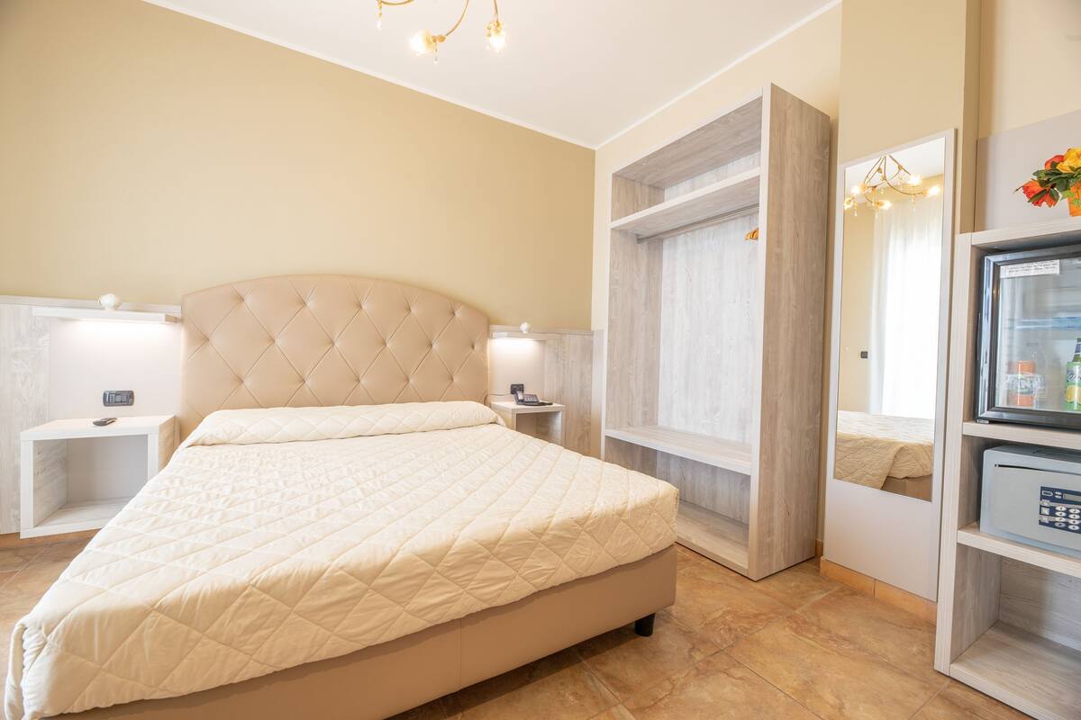 Un dormitorio con una cama grande, mesitas de noche, armario empotrado y minibar.