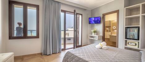 Ein modernes Hotelzimmer mit einem großen Bett, einem Fernseher, einem Balkon mit Aussicht und einem Badezimmer mit Spiegel und Waschbecken.