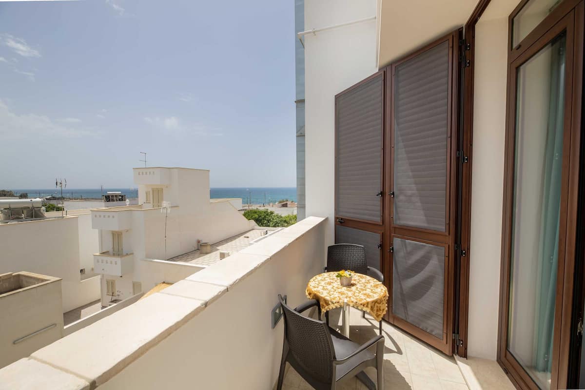 Un balcón con mesa y sillas, una puerta corrediza de vidrio y vista al mar.