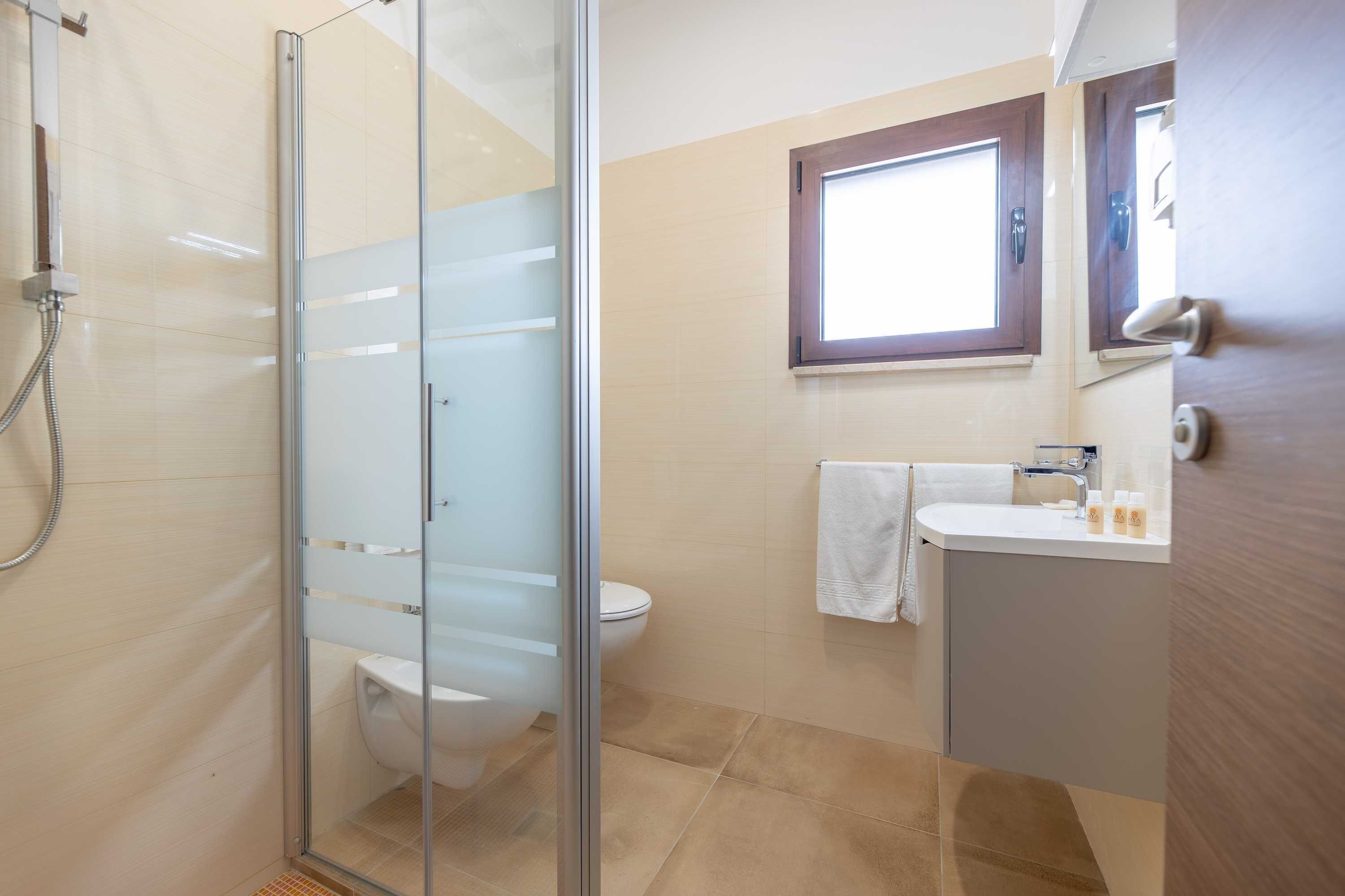 A modern bathroom with a glass shower enclosure, a toilet, a sink with a mirror, and a window.