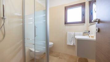 A modern bathroom with a glass shower enclosure, a toilet, a sink with a mirror, and a window.