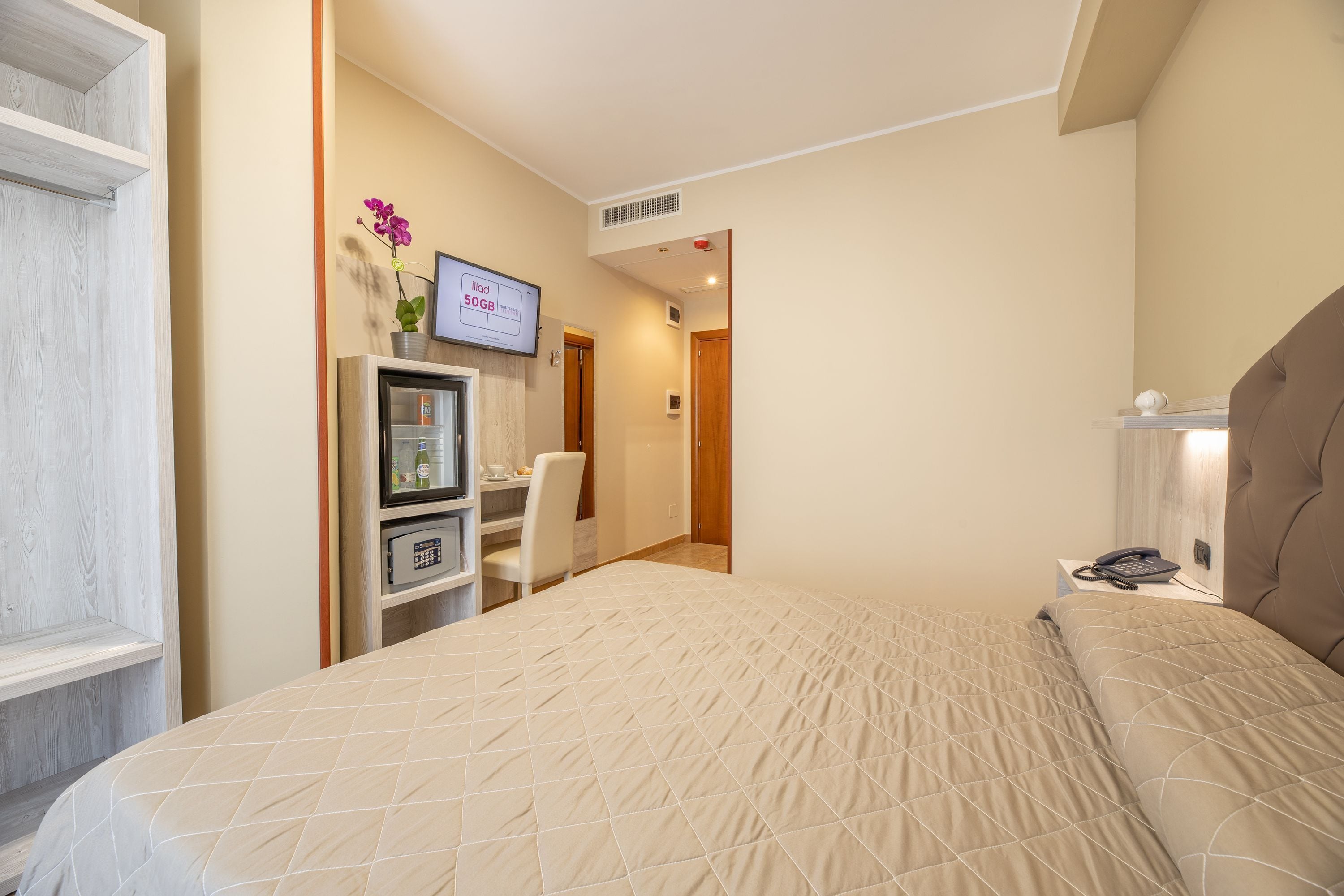 Habitación de hotel con cama, escritorio, computadora, teléfono, televisor y una pequeña mesa con una silla.