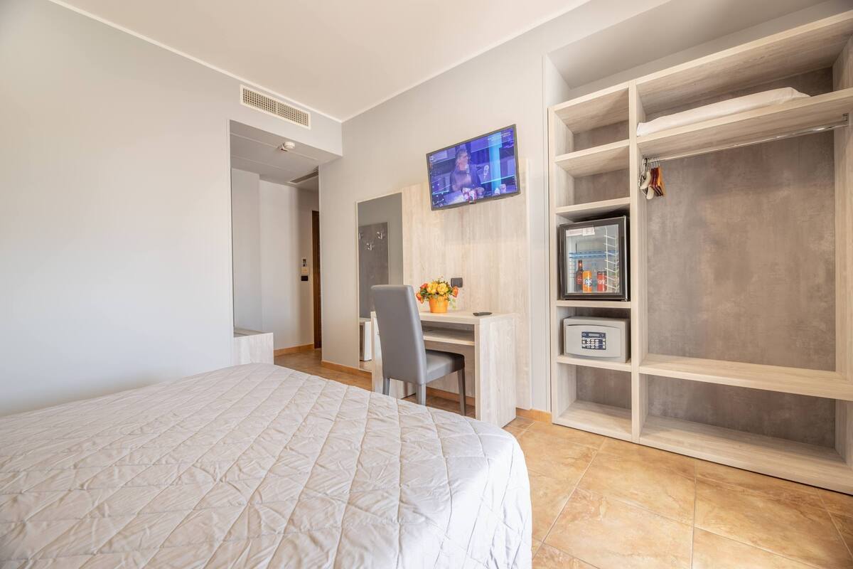 Una habitación de hotel con cama, escritorio con computadora, televisor y armario.