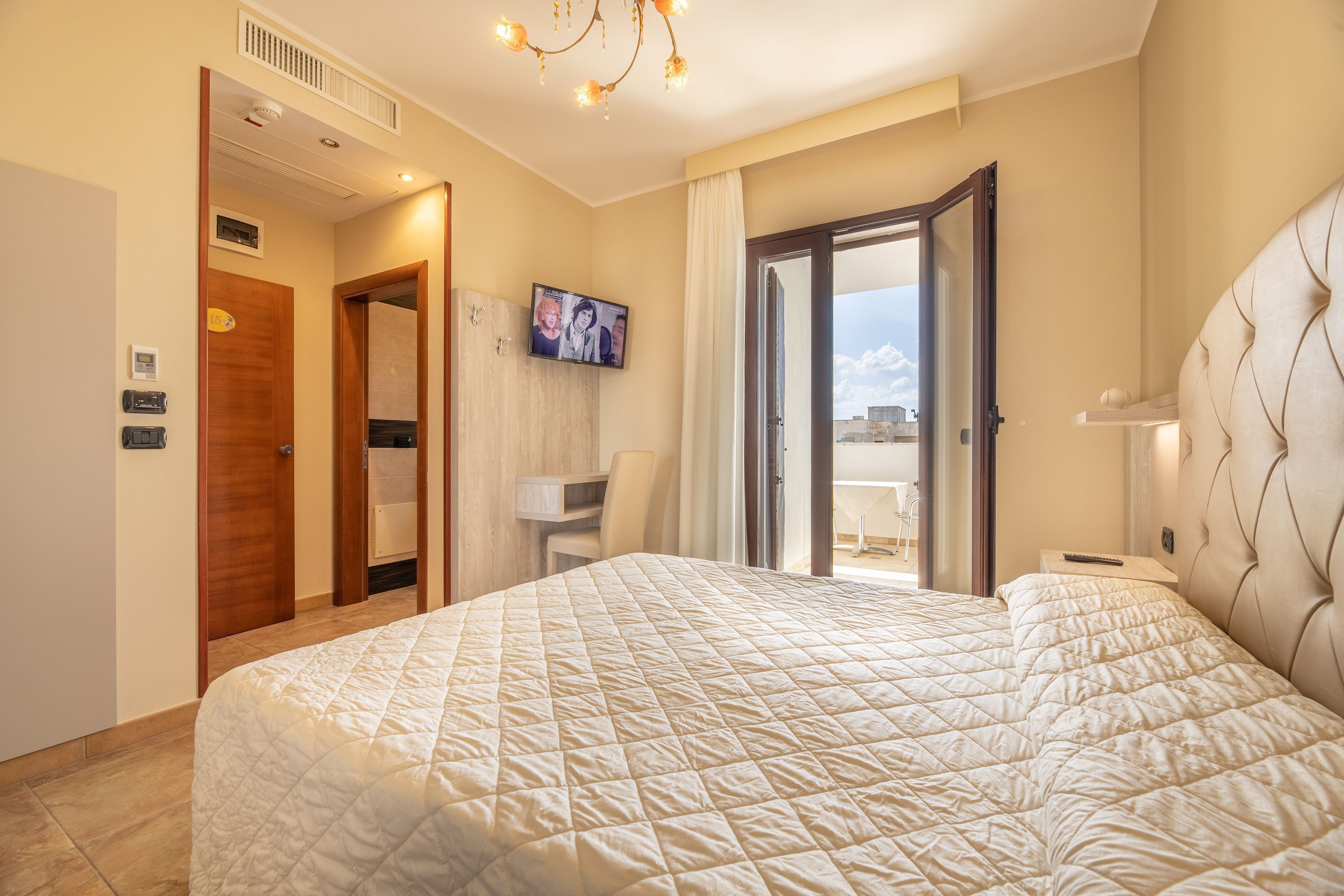 A hotel room with a large bed, a television on the wall, a desk, and a view of the outside.