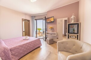 A hotel room with a bed, a chair, a TV, a minibar, and a balcony with a view.
