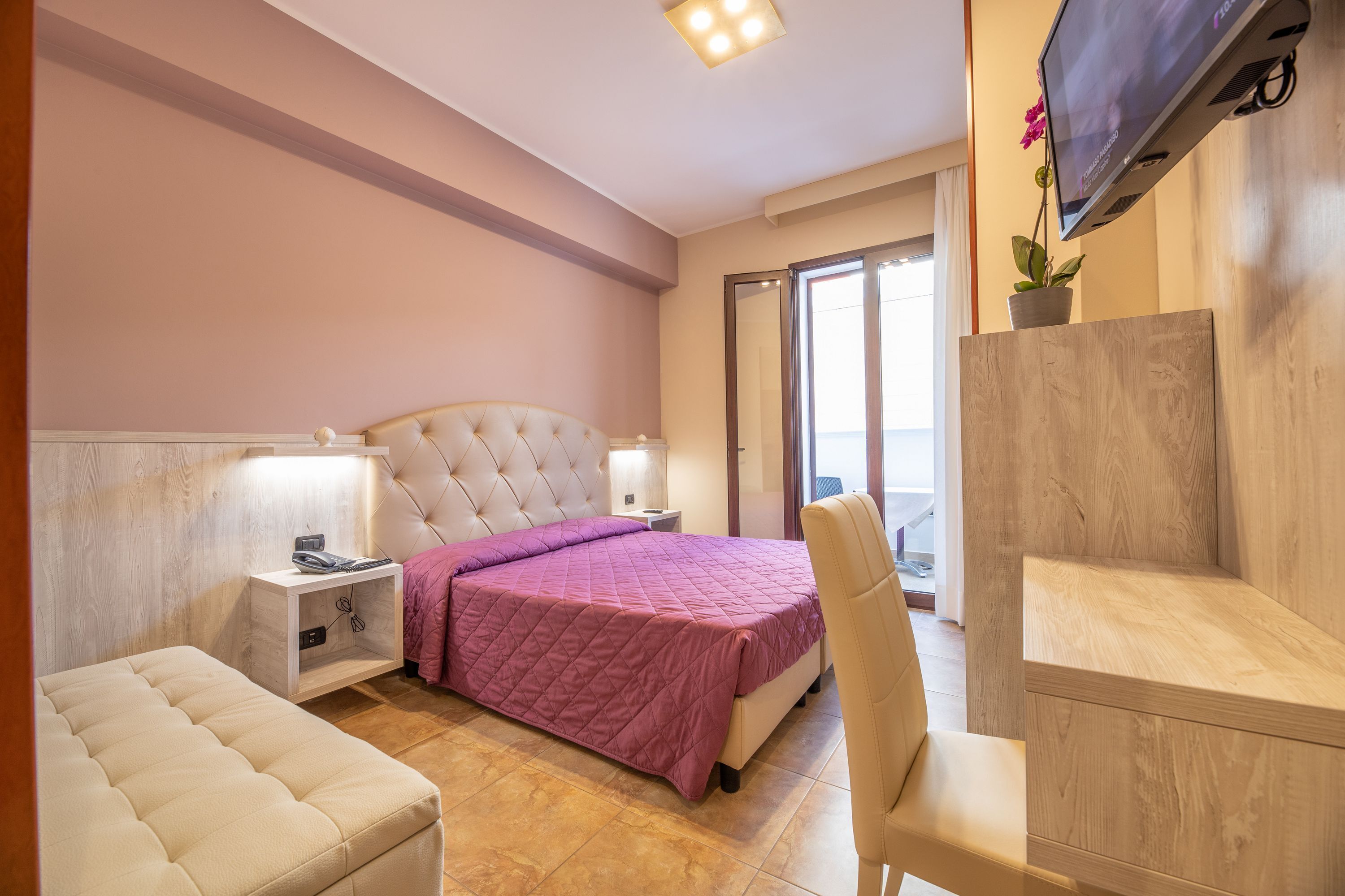 Ein Schlafzimmer mit einem Bett, Nachttischen, einem Sessel, einem Schreibtisch und einem Fernseher.