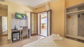 A hotel room with a bed, a desk with a television, a mini-fridge, a chair, and a wardrobe.