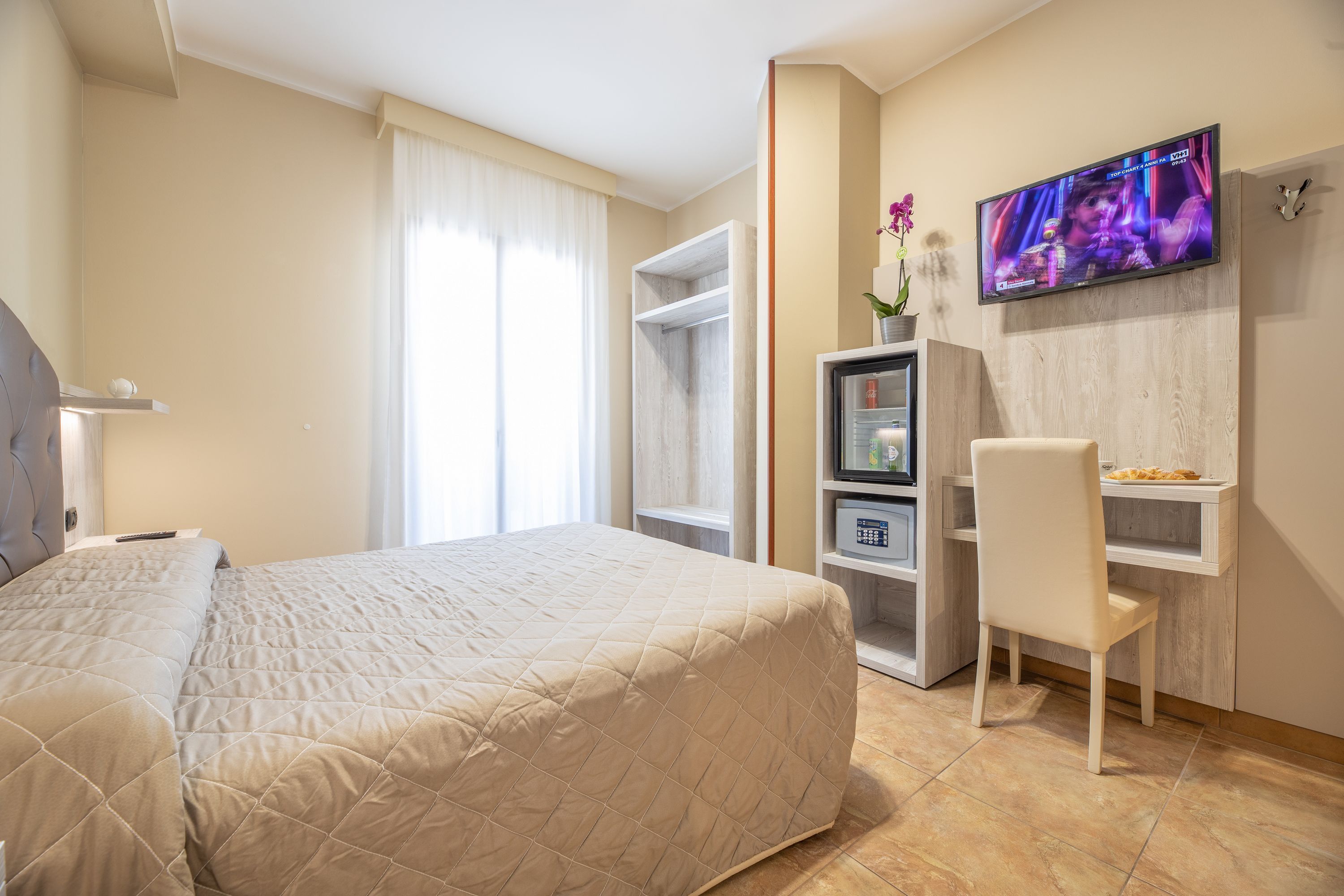 Een hotelkamer met een groot bed, een aan de muur bevestigde televisie, een bureau met een stoel en een kledingkast.