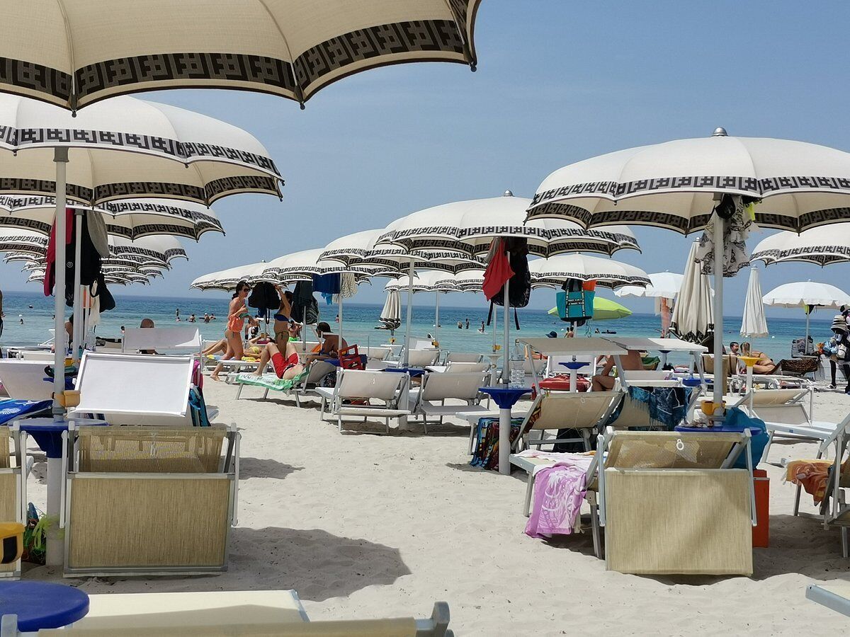 A beach with rows of sunbeds and umbrellas, some with people sitting under them.