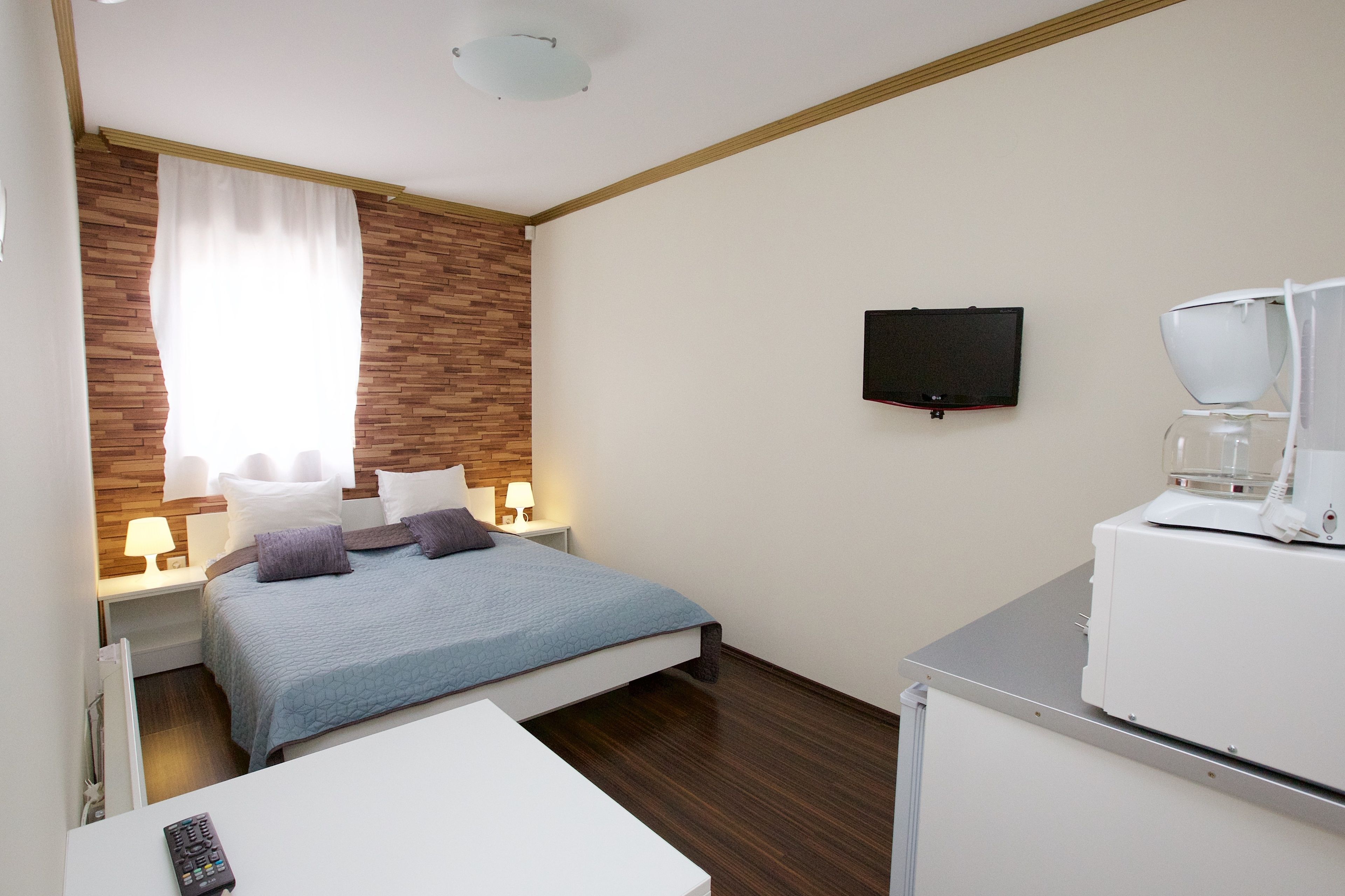 Een hotelkamer met een bed, een bureau, een koffiezetapparaat, een televisie en een raam met gordijnen.