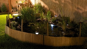 A garden pond with a wooden border, surrounded by various plants and rocks. - Sunset Apartments (Hajduszoboszlo)