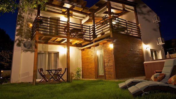 A two-story wooden house with a balcony, outdoor seating, and a hot tub. - Sunset Apartments (Hajduszoboszlo)