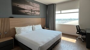 A modern hotel room with a large bed, a desk, a chair, and a view of the city.