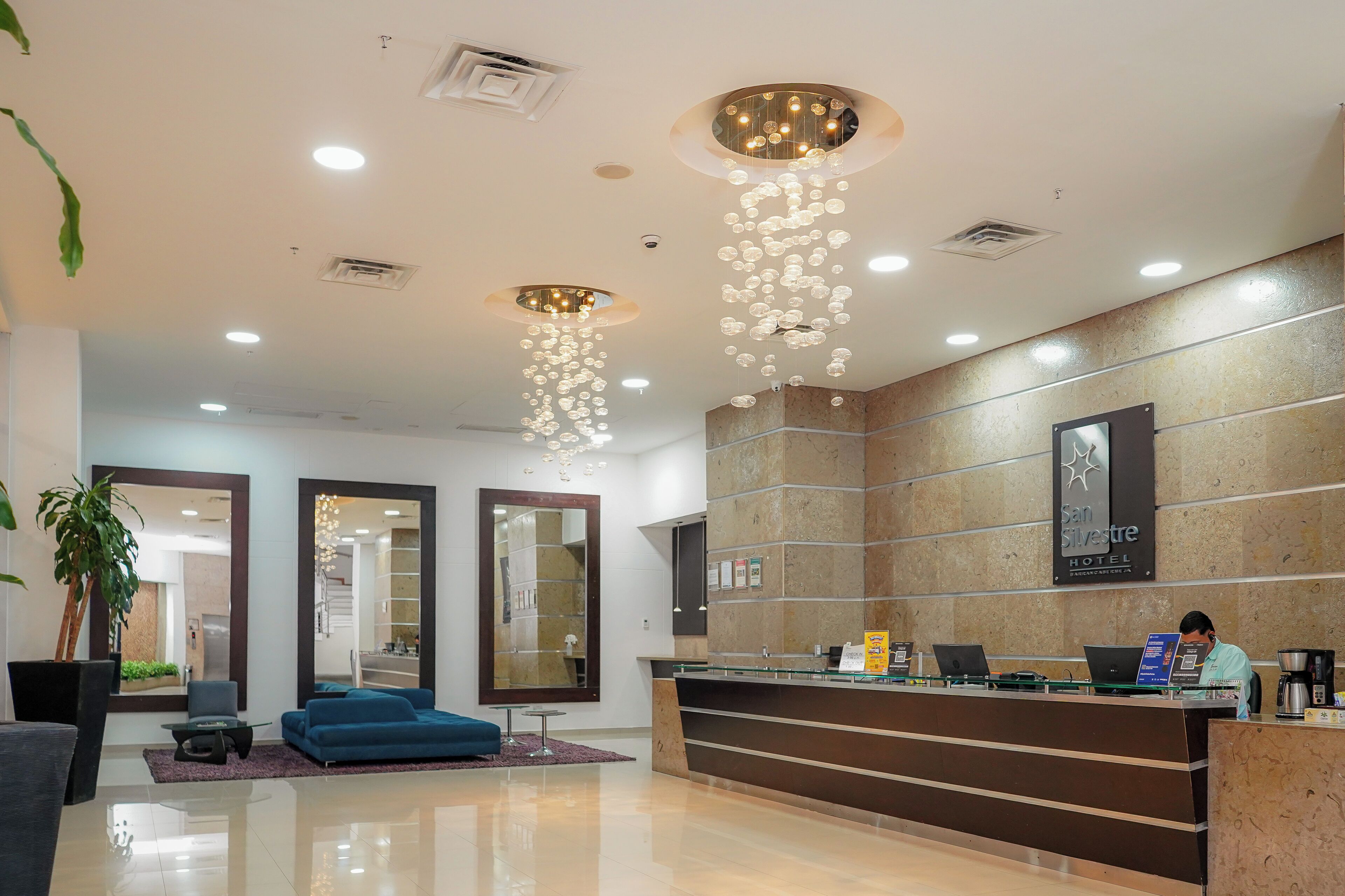 A hotel reception area with a modern design, including a reception desk, seating area, and decorative lighting fixtures.