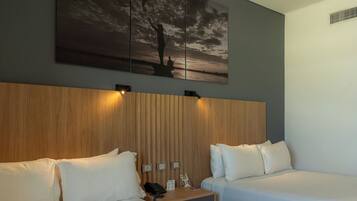 Habitación de hotel con dos camas, cabecera de madera, mesita de noche con teléfono y un cuadro de un atardecer.