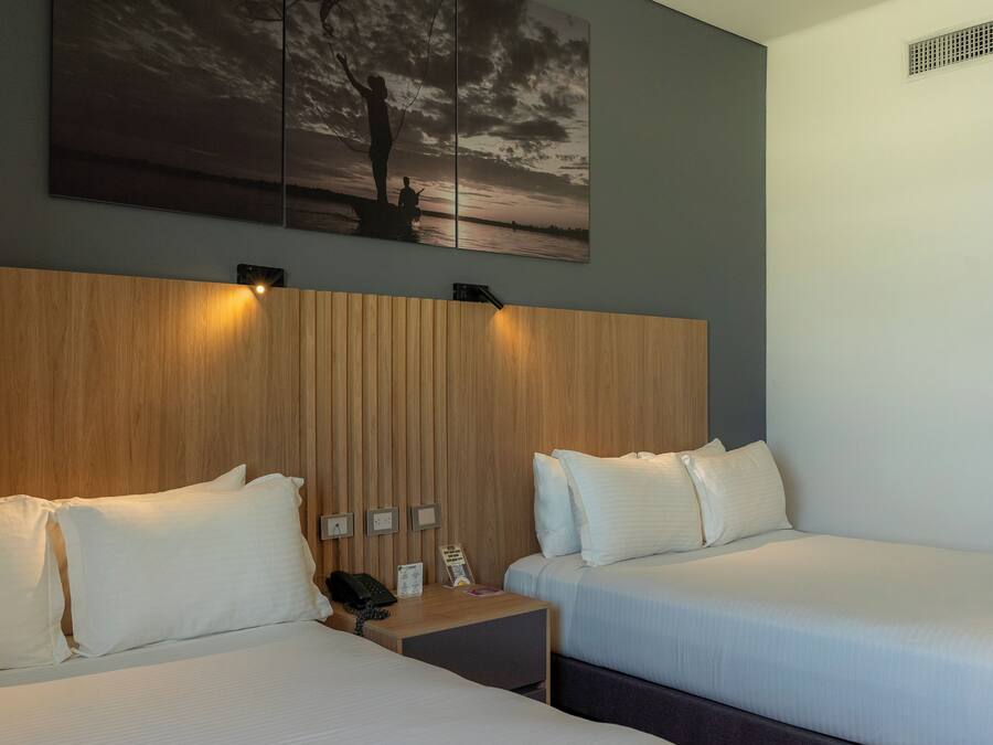 Habitación de hotel con dos camas, cabecera de madera, mesita de noche con teléfono y un cuadro de un atardecer.