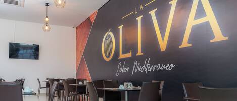 A modern dining area with a large wall sign reading 'OLIVA' and 'Sabor Mediterraneo'.