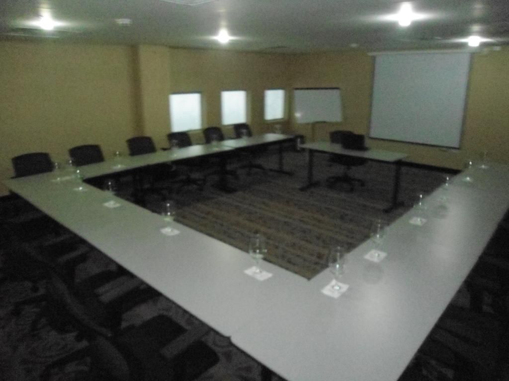 Un salón de conferencias con una larga mesa, sillas, una pantalla de proyector y suelo alfombrado.