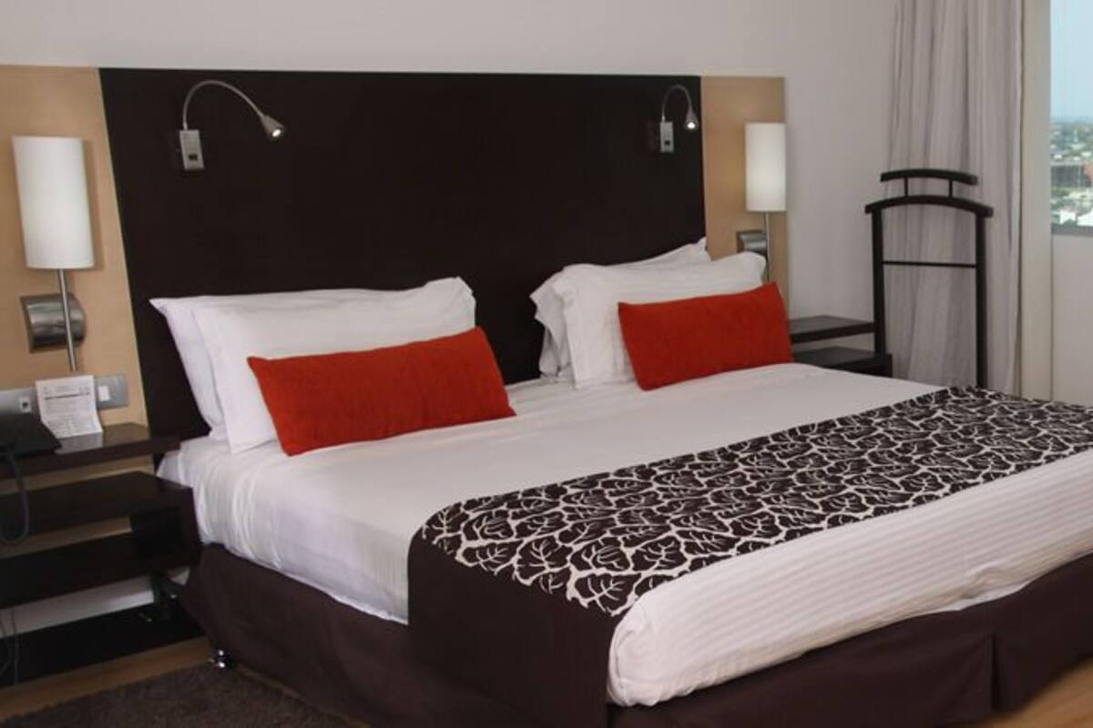 Habitación de hotel con una cama grande, dos mesitas de noche, un escritorio, una silla y vistas a la ciudad.