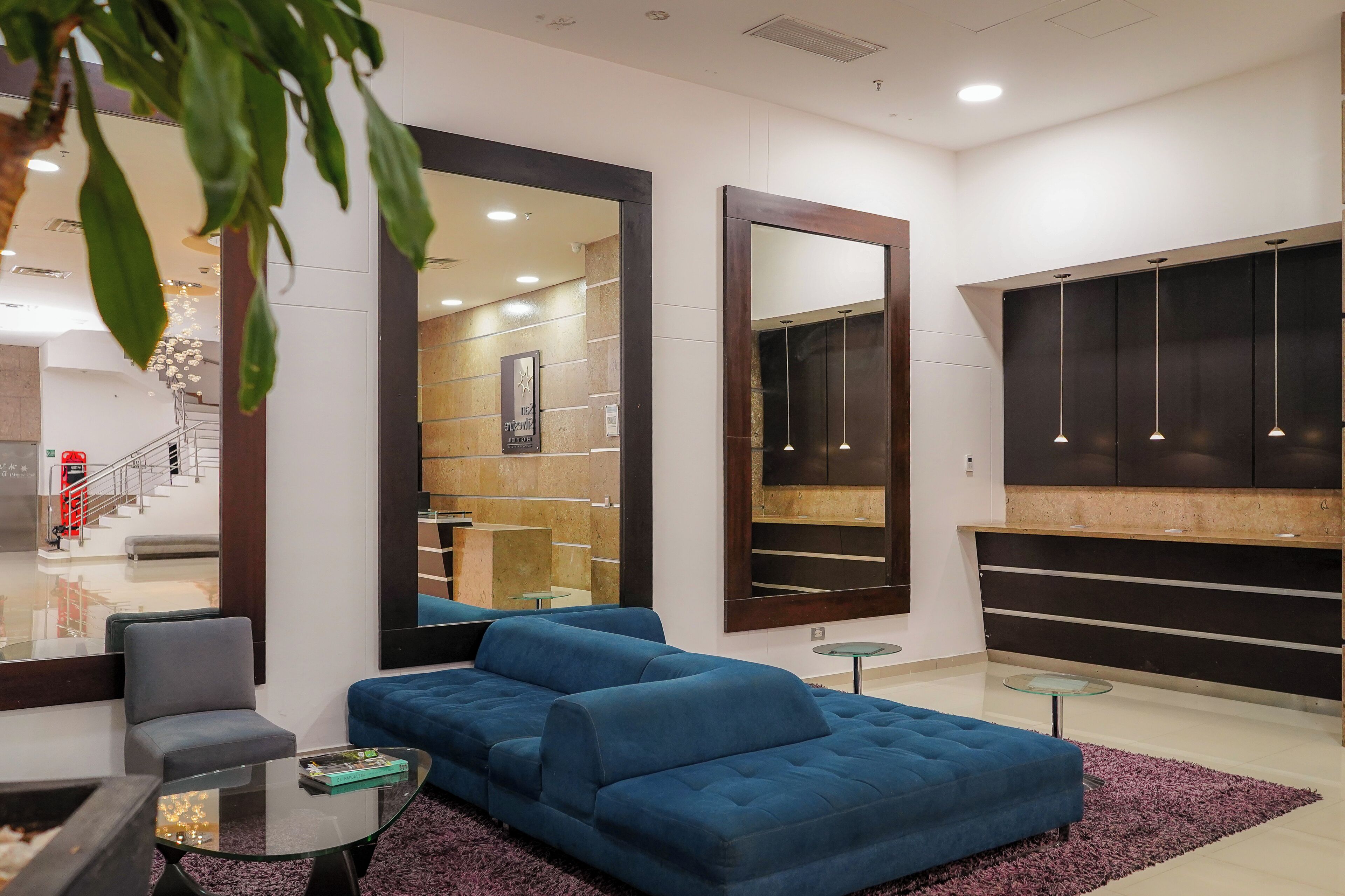 A modern living room with a blue sofa, a glass coffee table, and a large mirror.